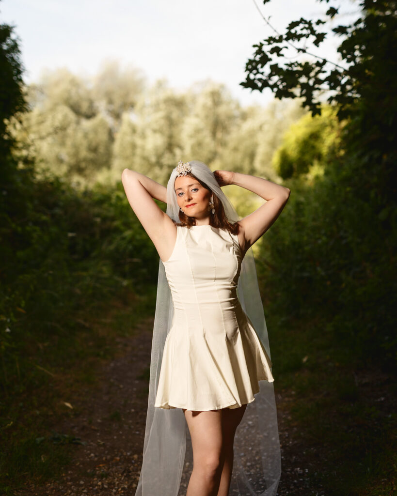 Sophia in a short cream bridal dress and long veil on a tree-lined path in Halesworth, Suffolk