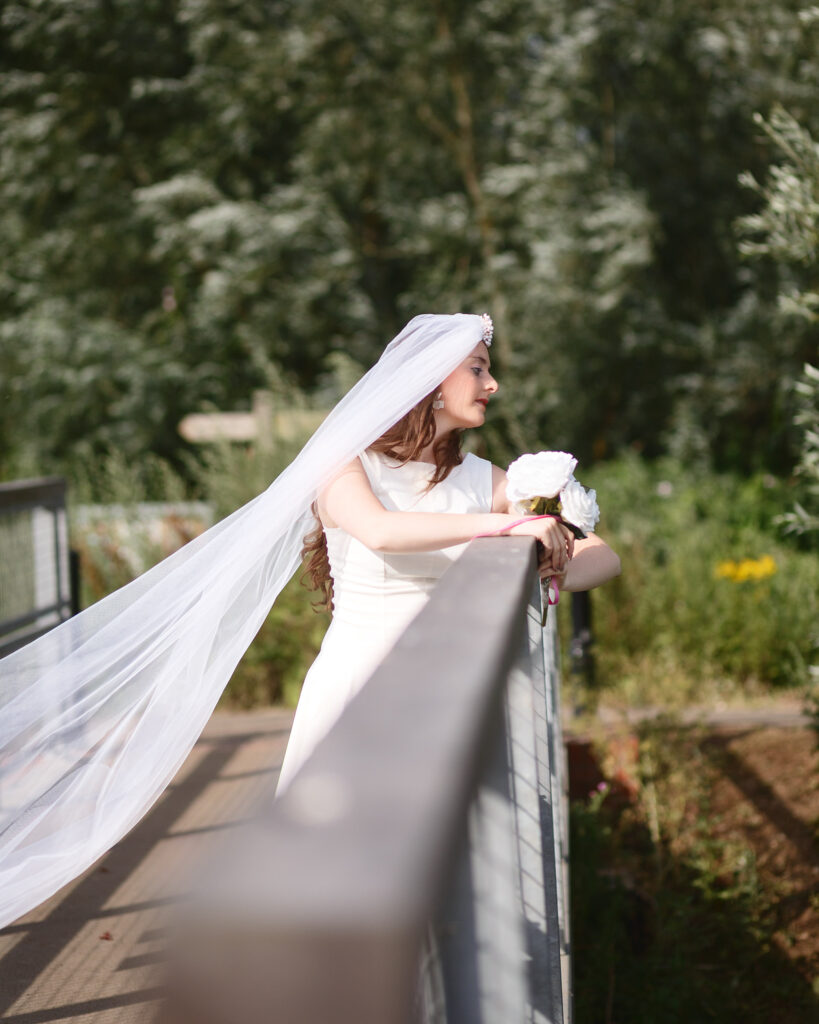Sophia leaning on a footbridge rail with her long veil caught in the breeze
