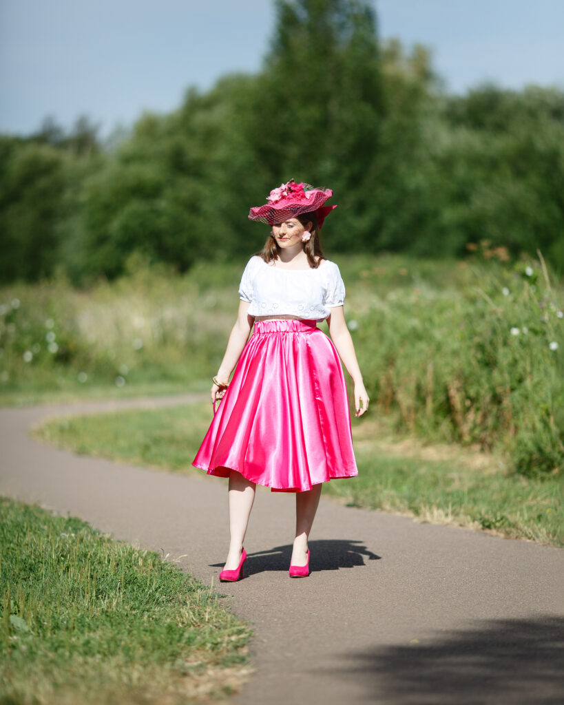 Sophia walking a Halesworth footpath in a fuchsia pink satin skirt, white top and pink hat