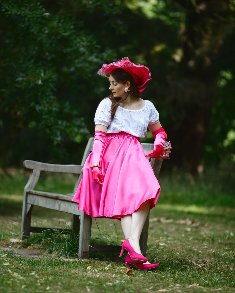 Sophia in pink satin and gloves resting against the arm of a park bench in dappled shade